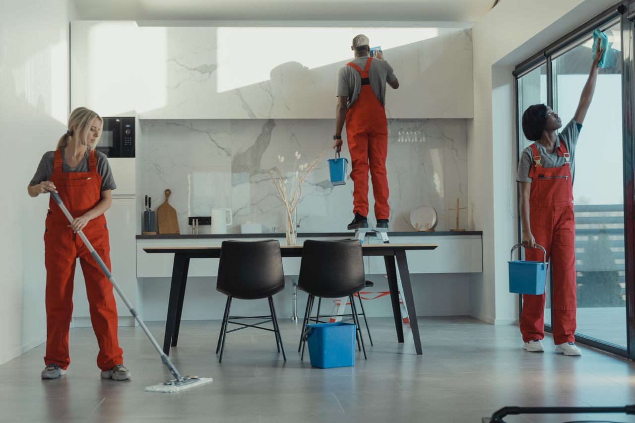 A team of cleaners in red uniforms is mopping and wiping the glass in a modern dining room.